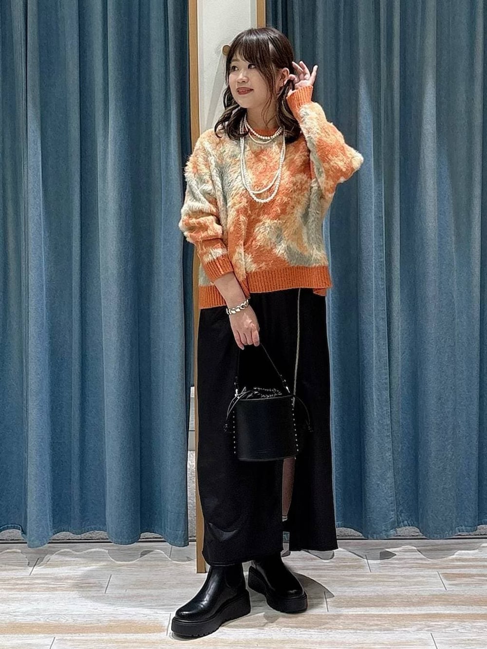ブラック系のブーツ、ブラック系のスカート、オレンジ系のニット/セーターを着用したレディースの冬コーディネートの4枚目の写真