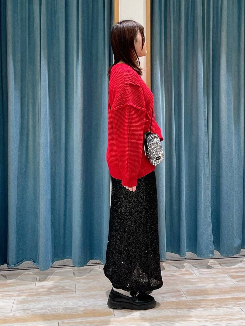 グレー系のショルダーバッグ、ブラック系のスカート、レッド系のニット/セーターを着用したレディースの冬コーディネートの2枚目の写真