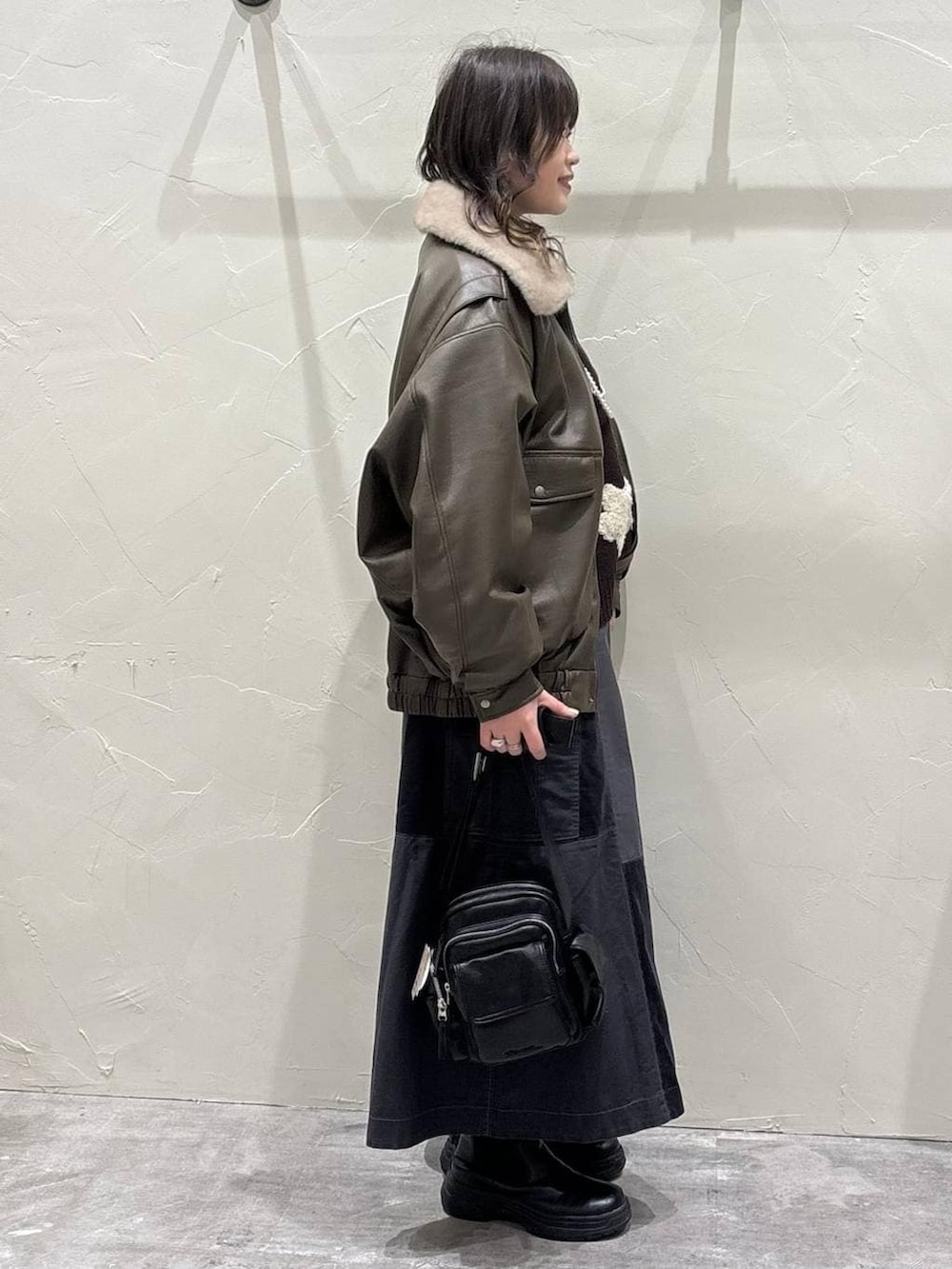 グレー系のスカート、ブラウン系のブルゾン、ブラック系のブーツを着用したレディースの冬コーディネートの2枚目の写真