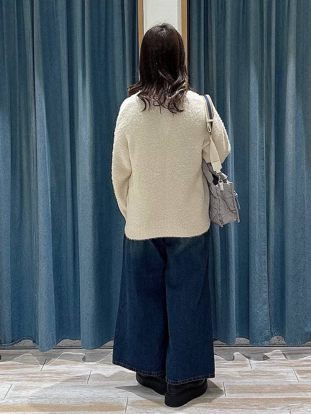 グレー系のショルダーバッグ、ブラック系のブーツ、ブルー系のデニムパンツを着用したレディースの冬コーディネートの3枚目の写真