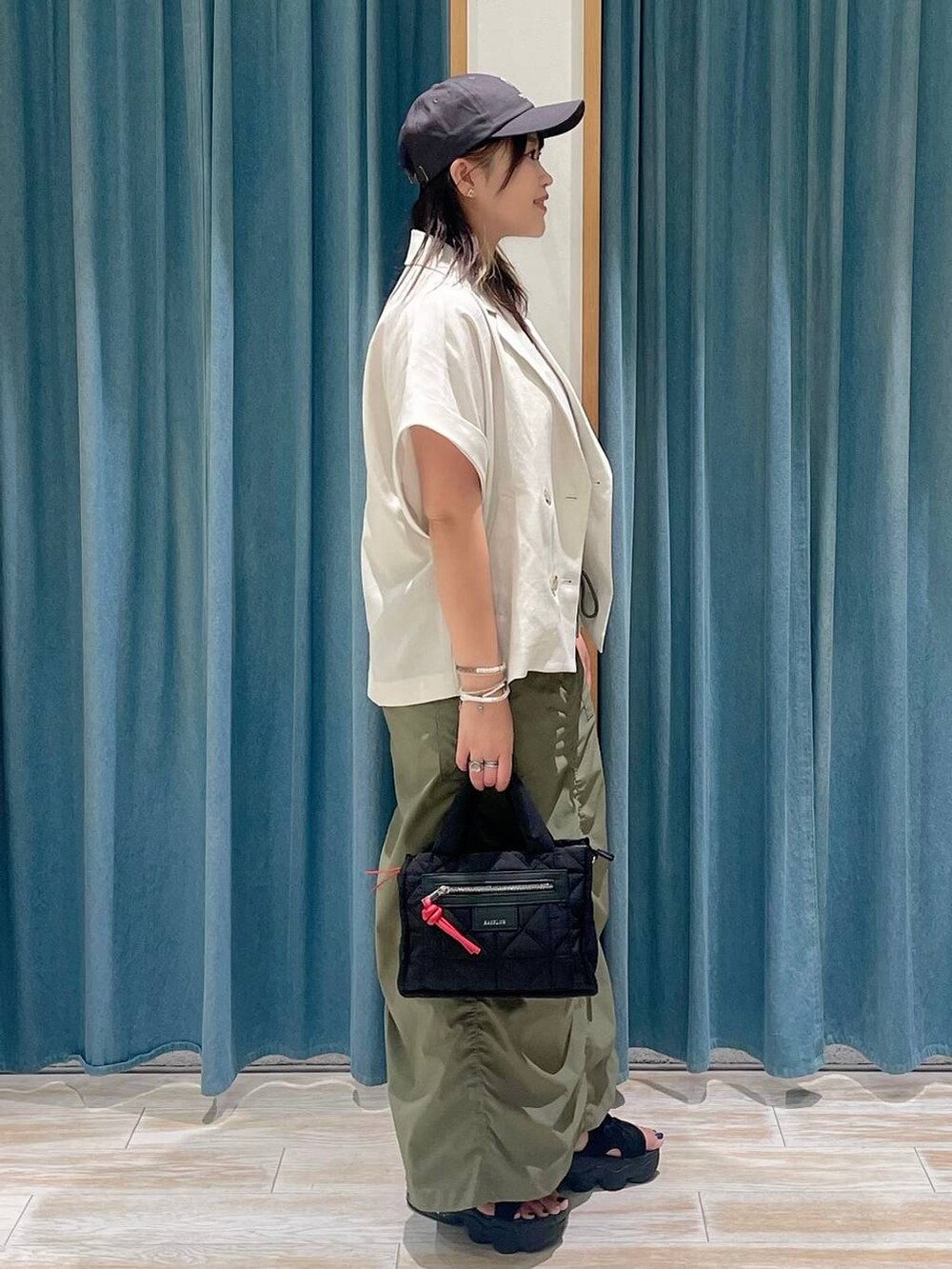 ホワイト系のキャミソール、ブラック系のショルダーバッグ、グリーン系のスカートを着用したレディースの夏コーディネートの2枚目の写真