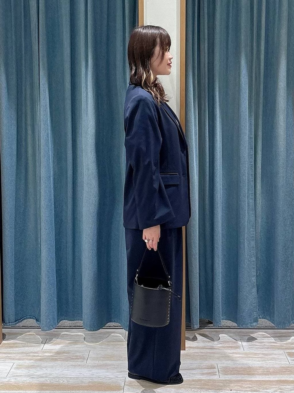 ブラック系のハンドバッグ、ブルー系のテーラードジャケット、ブルー系のスラックスを着用したレディースの冬コーディネートの2枚目の写真