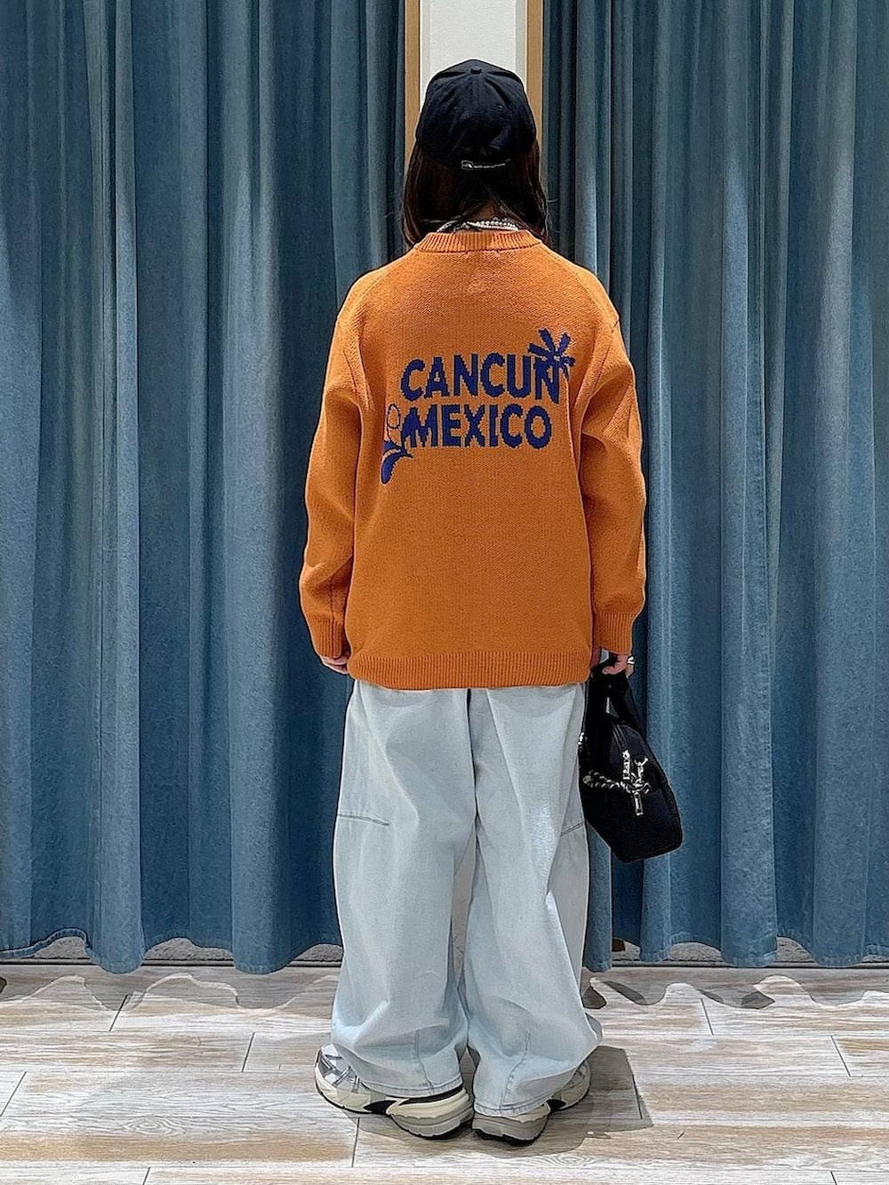 ブラック系のボストンバッグ、オレンジ系のニット/セーター、ブルー系のデニムパンツを着用したレディースの冬コーディネートの3枚目の写真