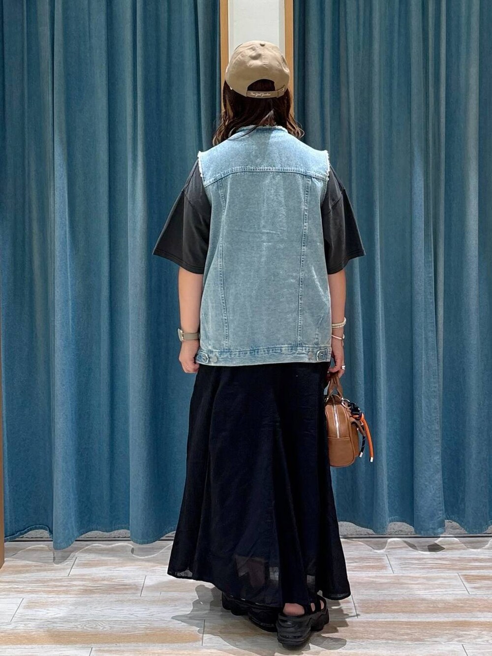 ブラック系のスカート、ブルー系のベスト、ブラウン系のボストンバッグを着用したレディースの夏コーディネートの3枚目の写真