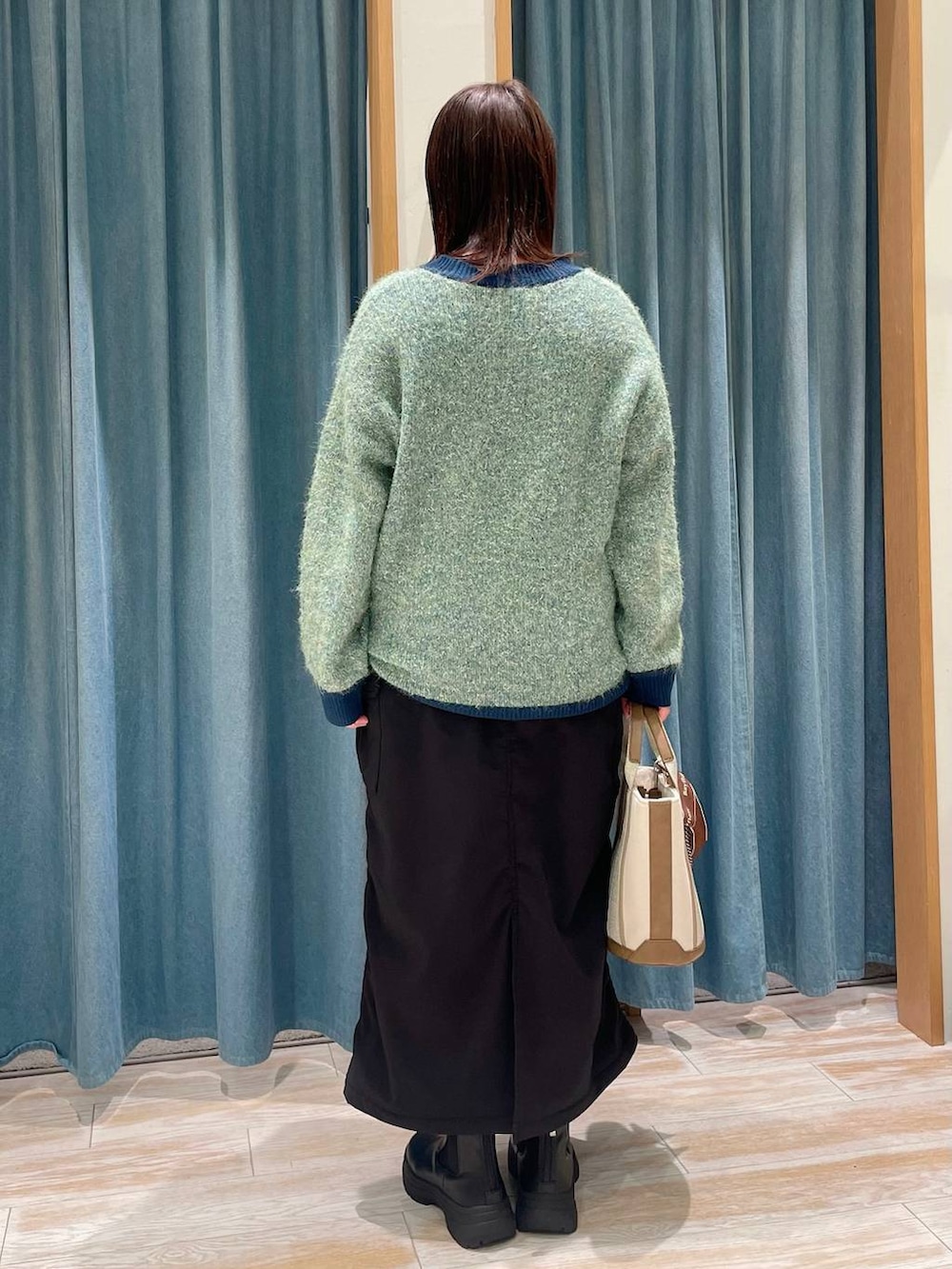 ブラック系のスカート、ブラック系のブーツ、グリーン系のニット/セーターを着用したレディースの冬コーディネートの2枚目の写真