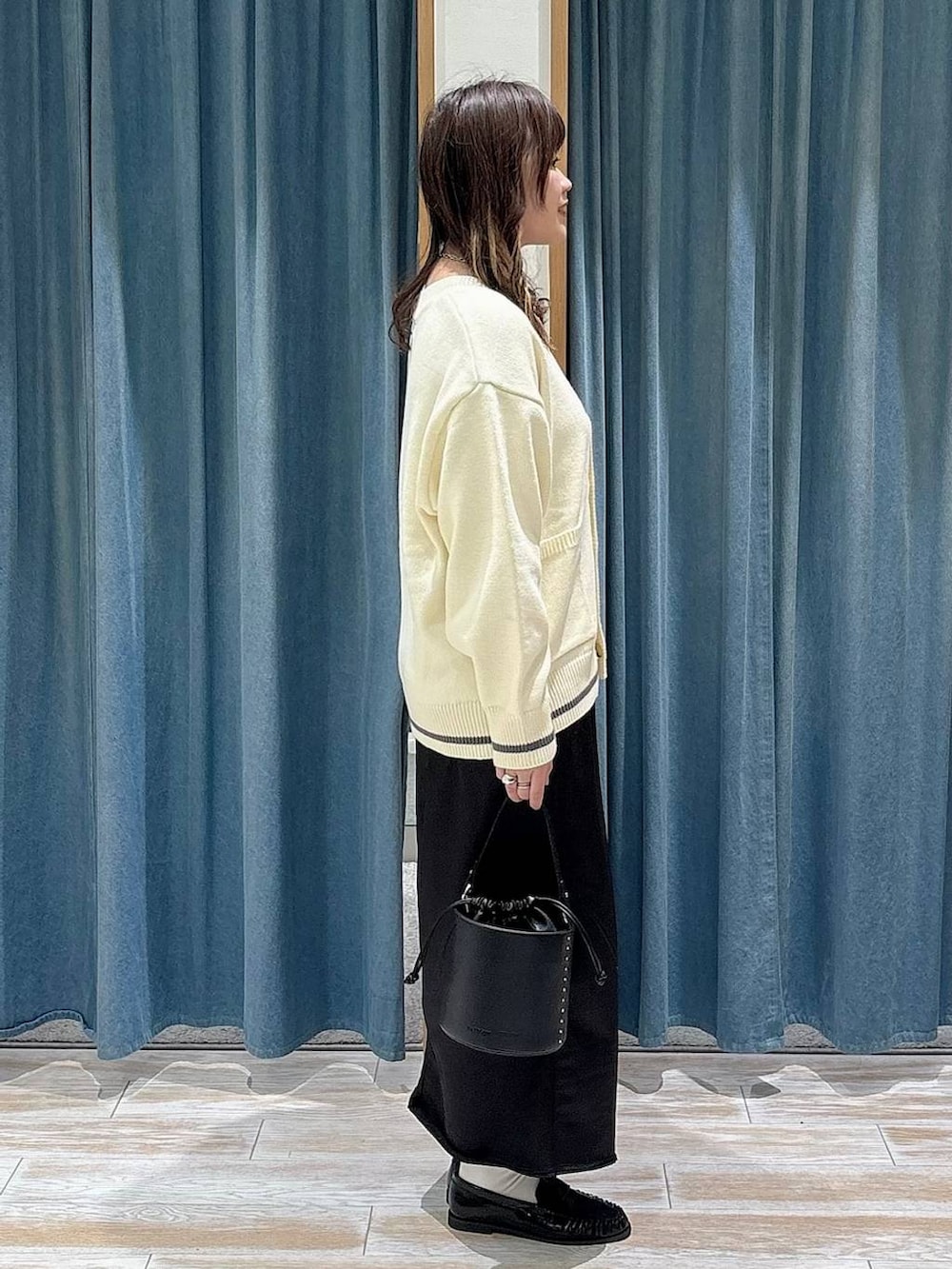 ブラック系のスカート、ホワイト系のカーディガン/ボレロ、ブラック系のハンドバッグを着用したレディースの冬コーディネートの2枚目の写真