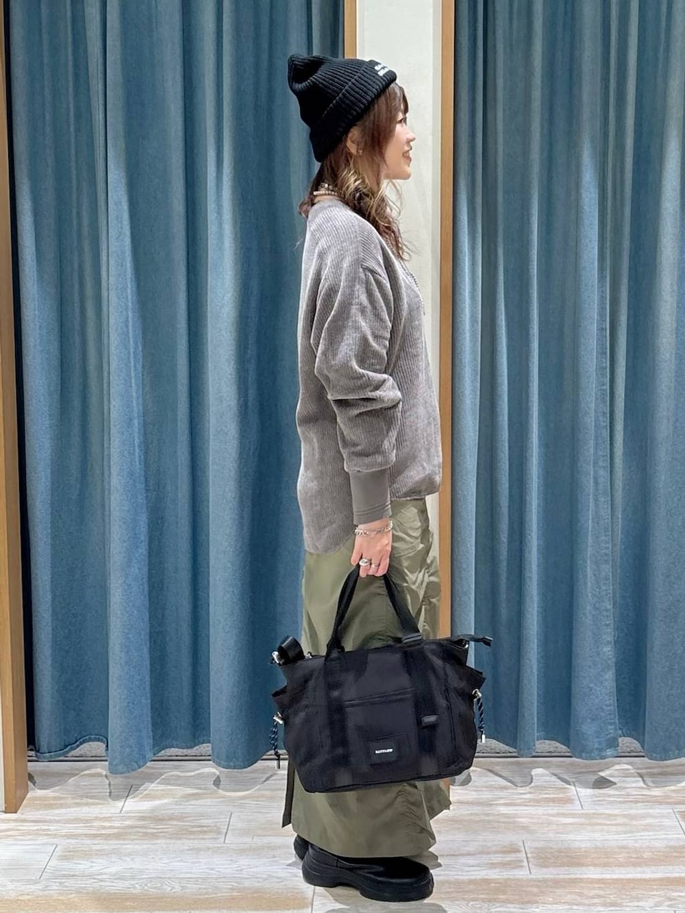 グリーン系のスカート、ブラック系のブーツ、ブラック系のトートバッグを着用したレディースの秋コーディネートの2枚目の写真