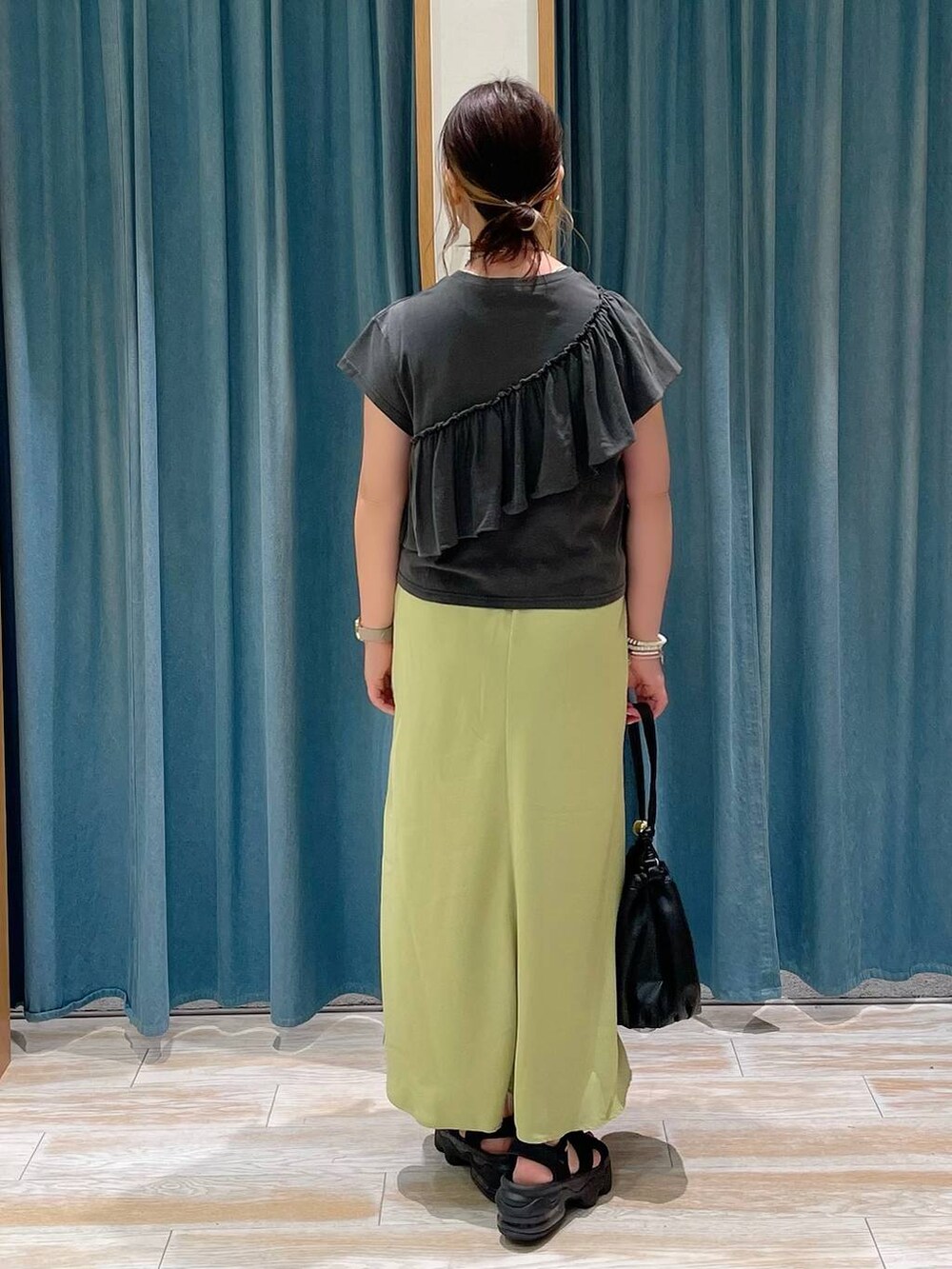 ブラック系のショルダーバッグ、グリーン系のスカート、グレー系のTシャツ/カットソーを着用したレディースの夏コーディネートの2枚目の写真