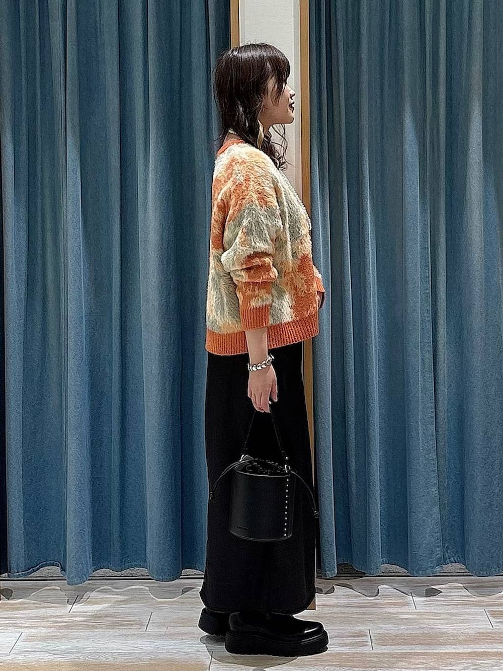 ブラック系のブーツ、ブラック系のスカート、オレンジ系のニット/セーターを着用したレディースの冬コーディネートの2枚目の写真