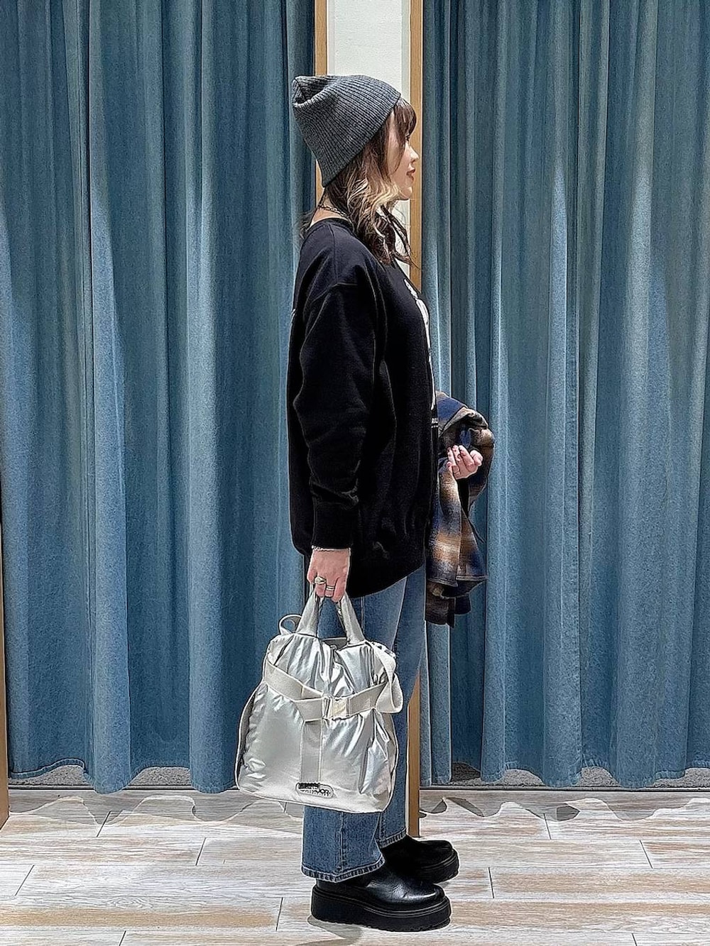 シルバー系のトートバッグ、ブルー系のデニムパンツ、ブラック系のスウェットを着用したレディースの冬コーディネートの2枚目の写真