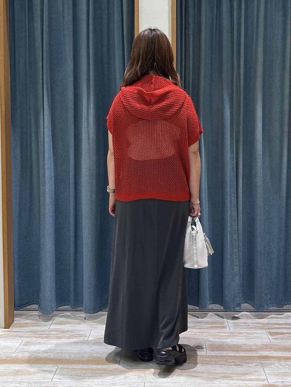 グレー系のショルダーバッグ、グレー系のスカート、レッド系のパーカーを着用したレディースの夏コーディネートの3枚目の写真