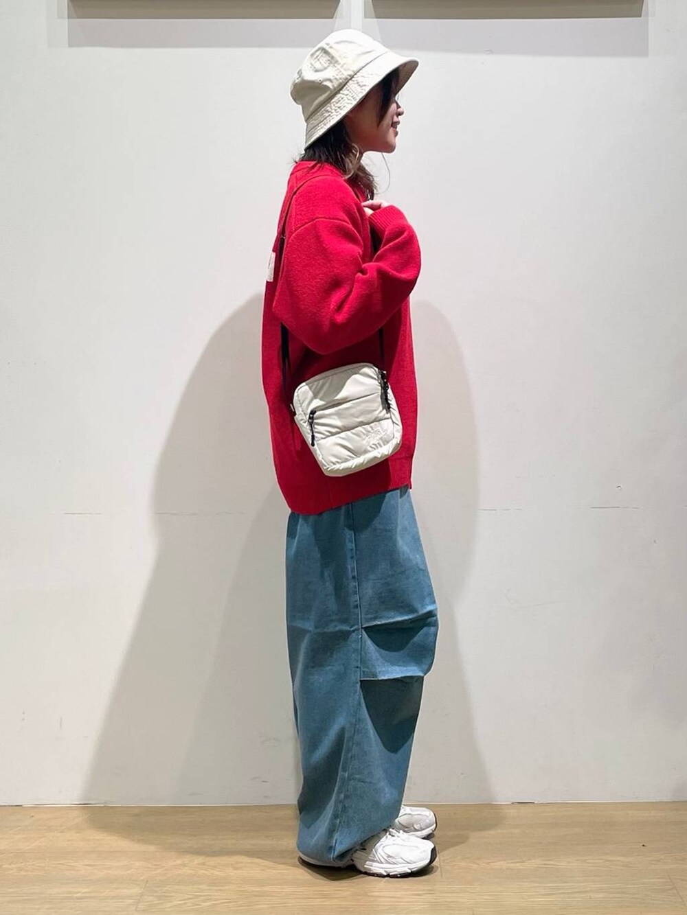 レッド系のニット/セーター、ブルー系のその他パンツ、ベージュ系のショルダーバッグを着用したレディースの秋コーディネートの2枚目の写真
