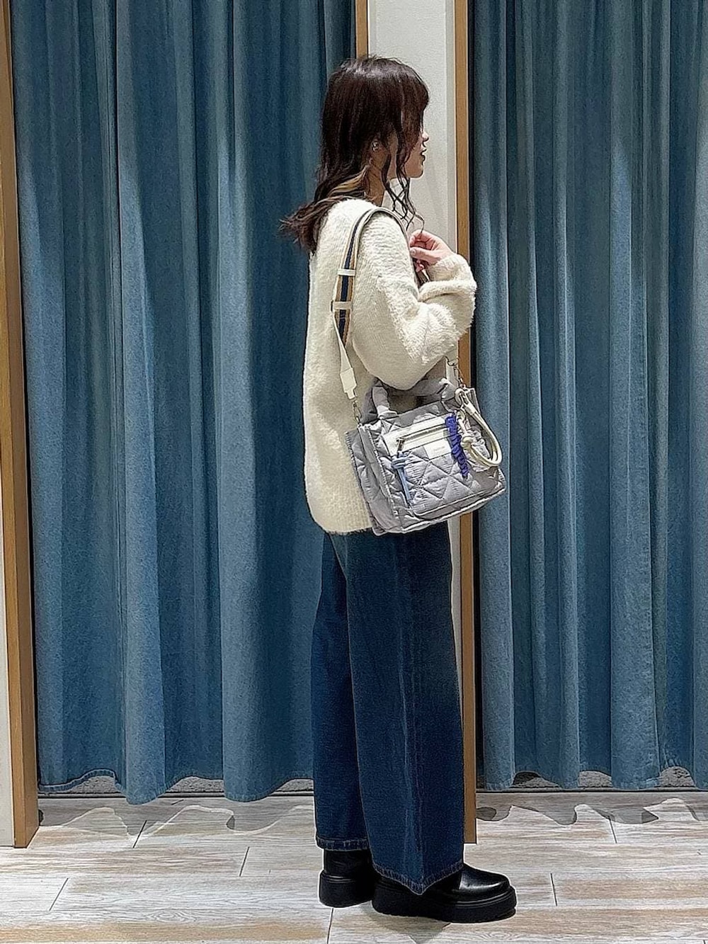 グレー系のショルダーバッグ、ブラック系のブーツ、ブルー系のデニムパンツを着用したレディースの冬コーディネートの2枚目の写真