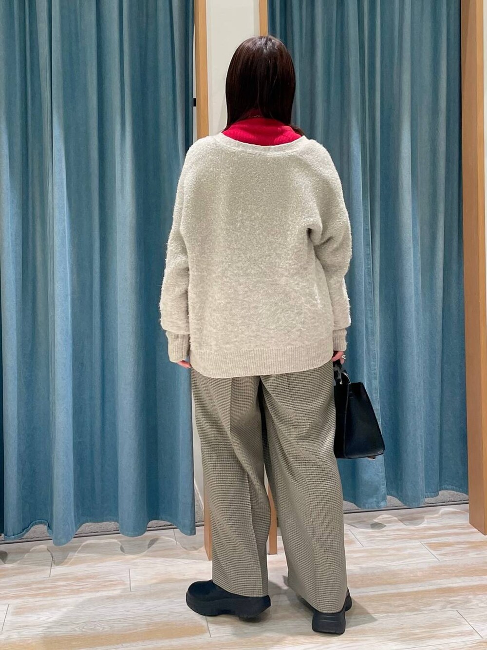 レッド系のニット/セーター、ブラック系のブーツ、ホワイト系のカーディガン/ボレロを着用したレディースの冬コーディネートの2枚目の写真