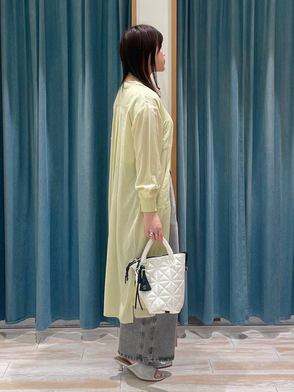 グレー系のデニムパンツ、イエロー系のシャツワンピース、シルバー系のサンダルを着用したレディースの春コーディネートの2枚目の写真