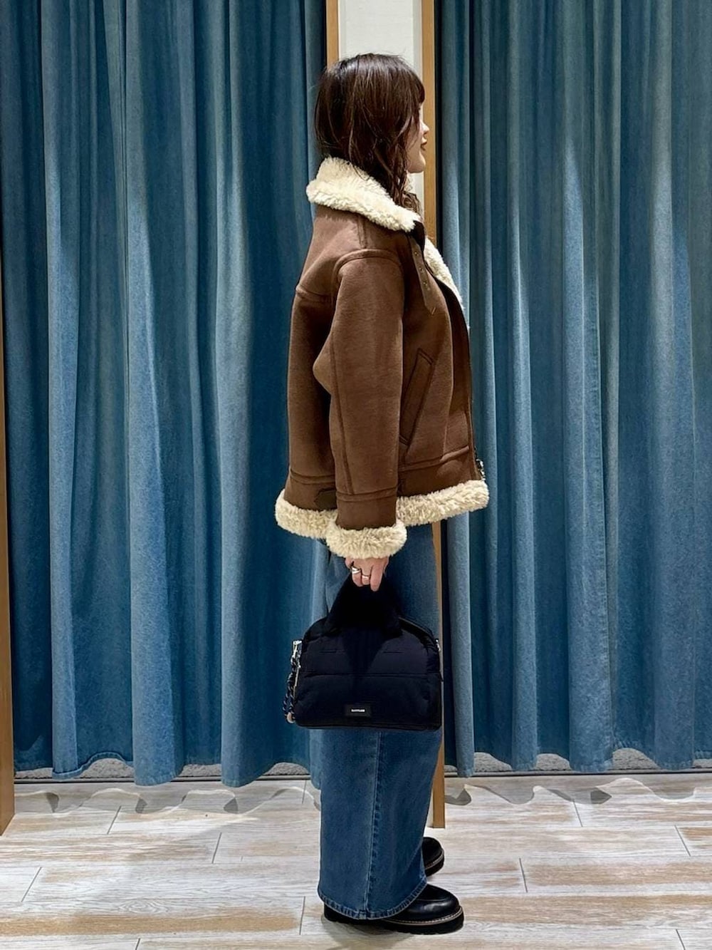 ブラック系のローファー、ブルー系のデニムパンツ、ブラック系のボストンバッグを着用したレディースの秋コーディネートの2枚目の写真