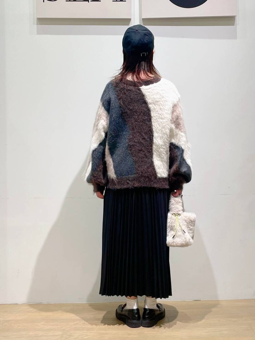 ブラウン系のニット/セーター、ブラック系のスカート、ホワイト系のショルダーバッグを着用したレディースの秋コーディネートの2枚目の写真