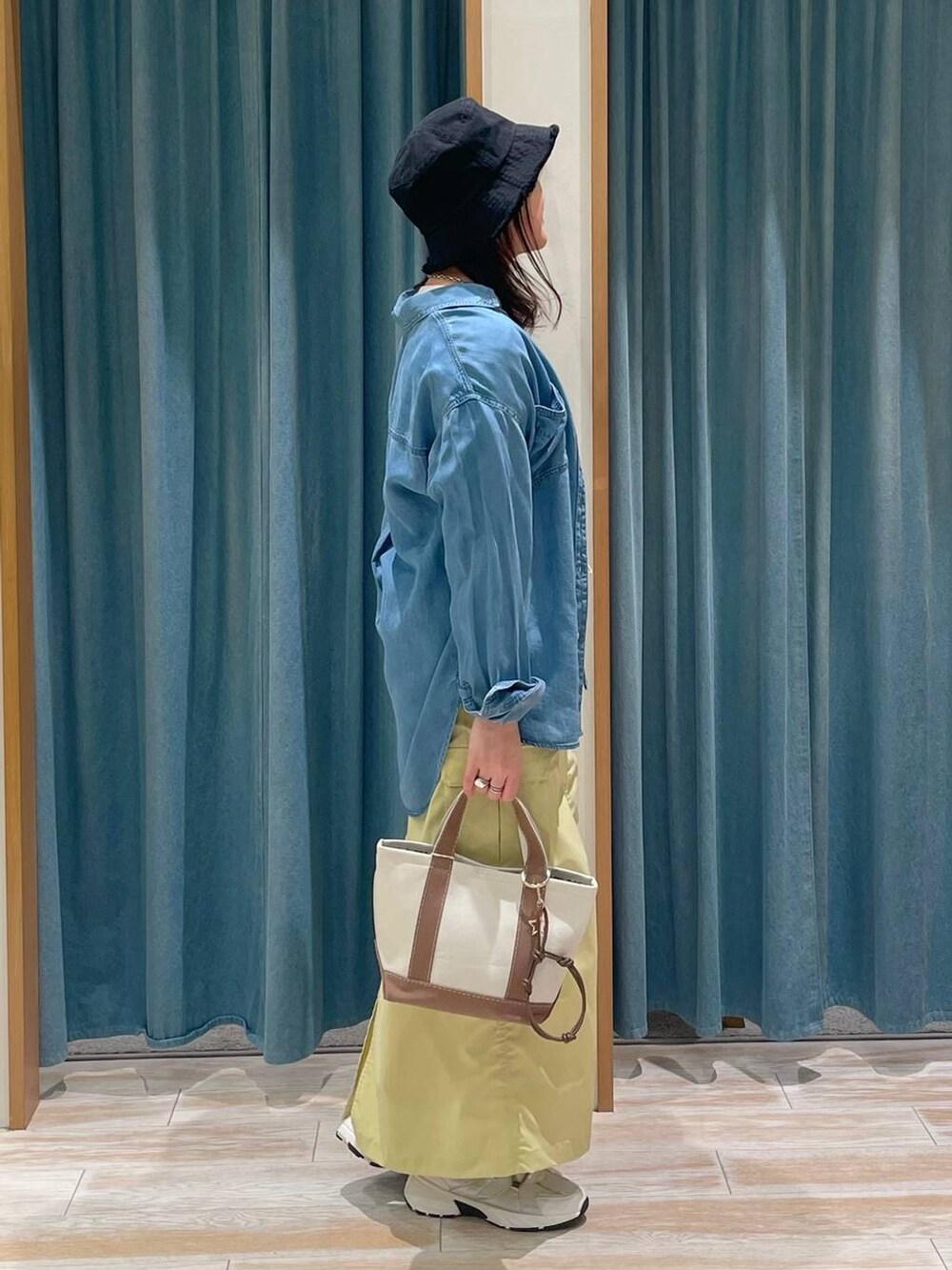 ブルー系のシャツ/ブラウス、ブラウン系のトートバッグ、ホワイト系のスニーカーを着用したレディースの春コーディネートの2枚目の写真