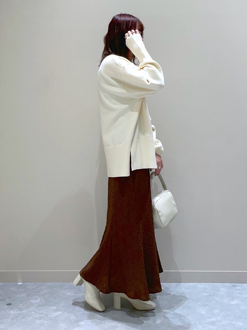 ホワイト系のニット/セーター、ブラウン系のスカート、ホワイト系のブーツを着用したレディースの冬コーディネートの2枚目の写真