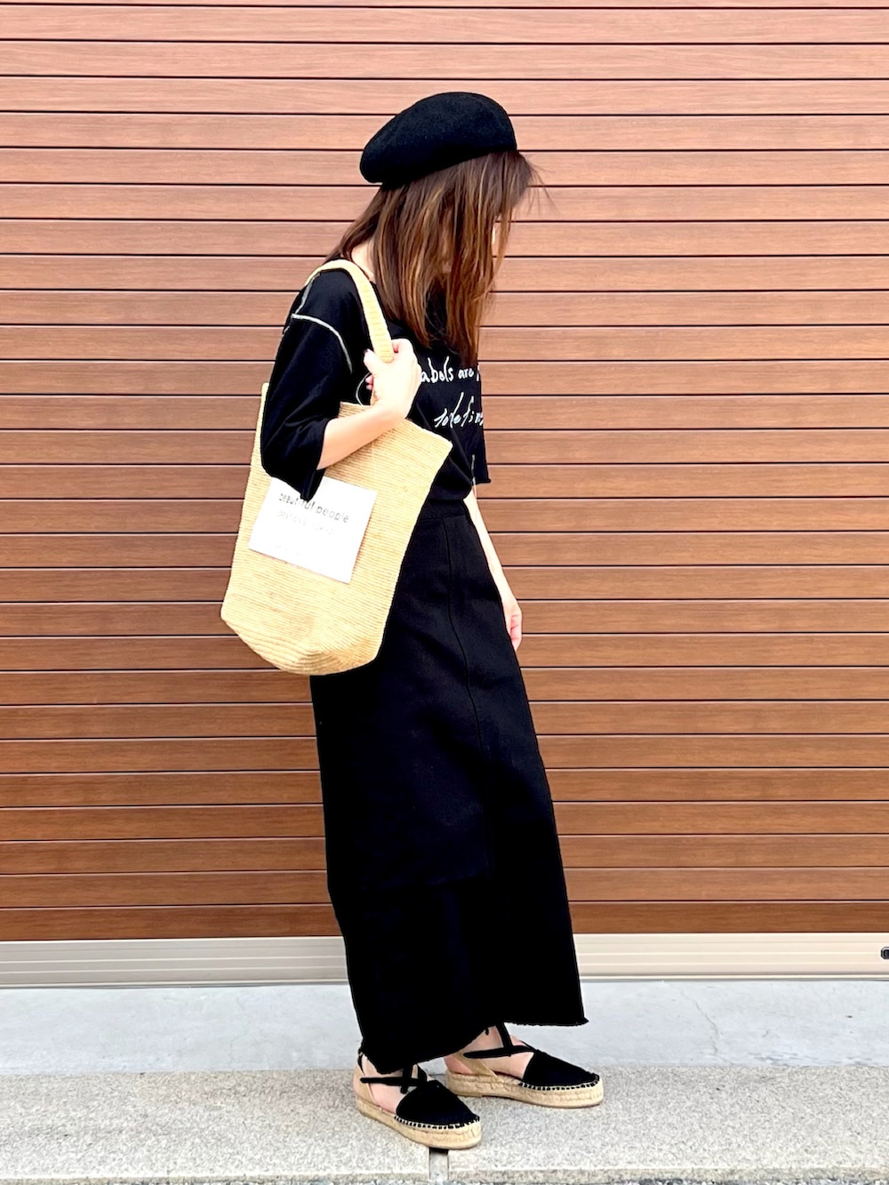 ベージュ系のトートバッグ、ブラック系のサンダル、ブラック系のTシャツ/カットソーを着用したレディースの夏コーディネートの4枚目の写真