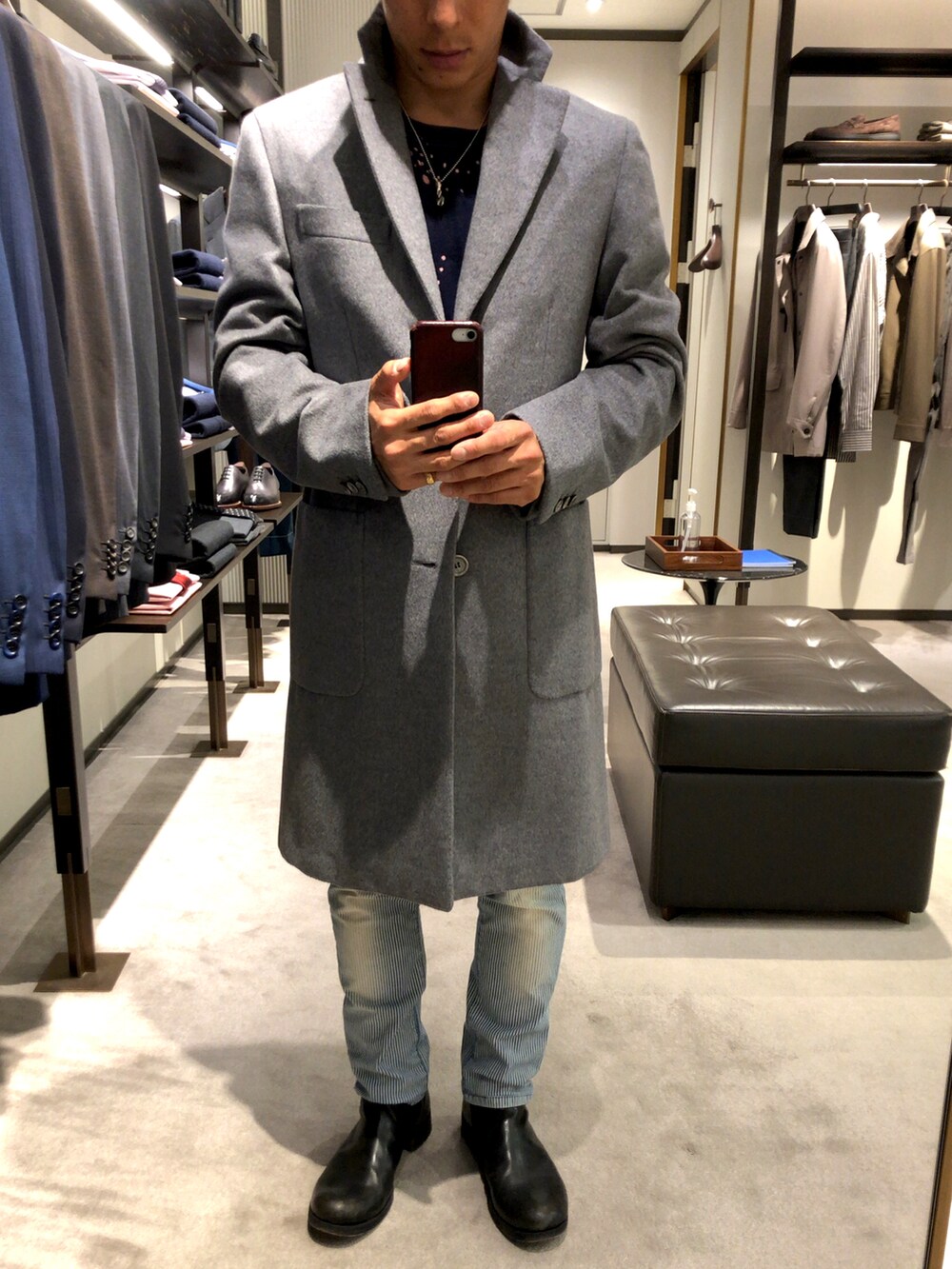 グレー系のチェスターコート、ブルー系のデニムパンツ、ブラック系のブーツを着用したメンズの秋コーディネートの2枚目の写真