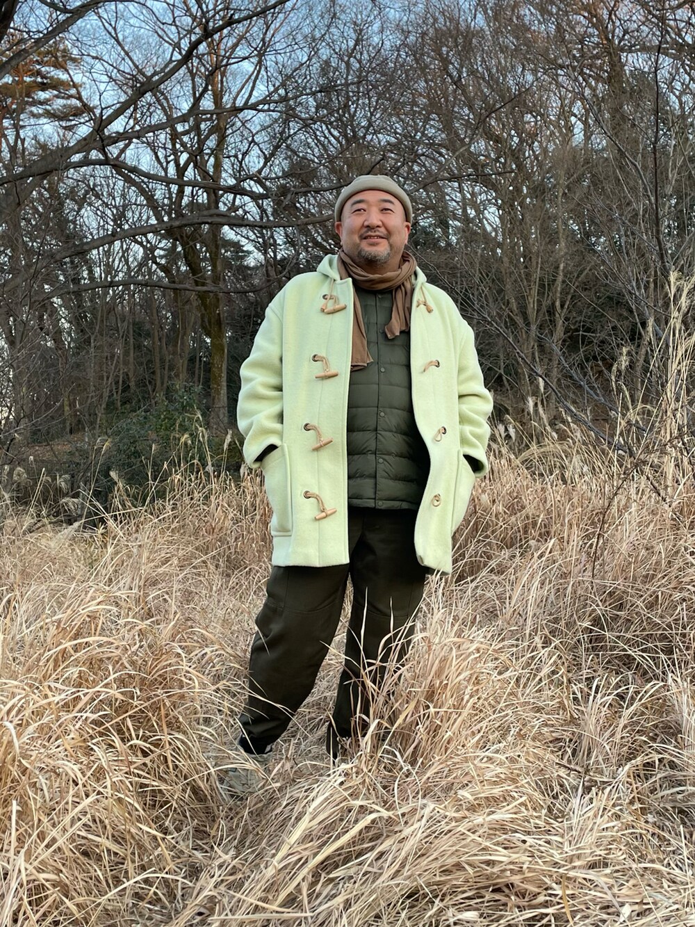 グリーン系のダッフルコート、ブラウン系のカーゴパンツ、ベージュ系のスニーカーを着用したメンズの冬コーディネートの2枚目の写真