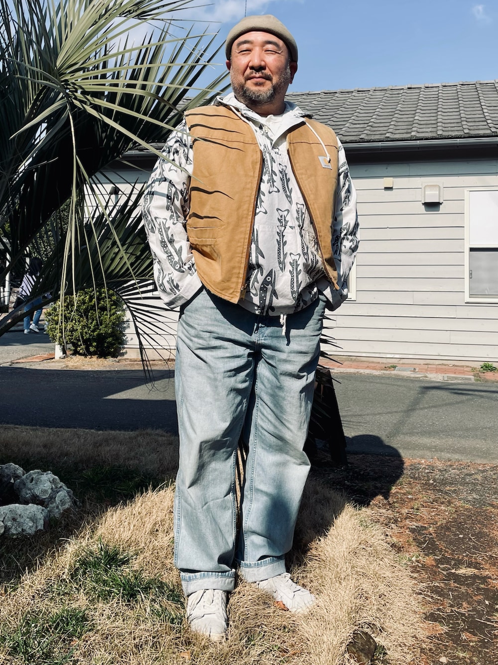 ブルー系のデニムパンツ、ホワイト系のスニーカー、ベージュ系のベストを着用したメンズの春コーディネートの2枚目の写真
