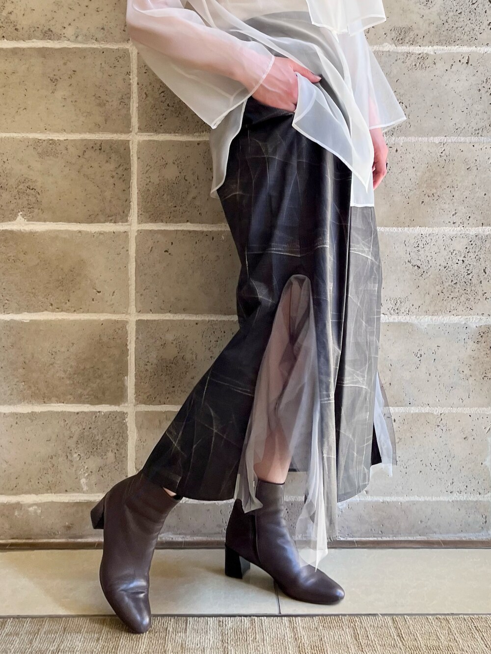 ブラック系のスカート、ブラウン系のブーツ、ホワイト系のタンクトップを着用したレディースの春コーディネートの3枚目の写真