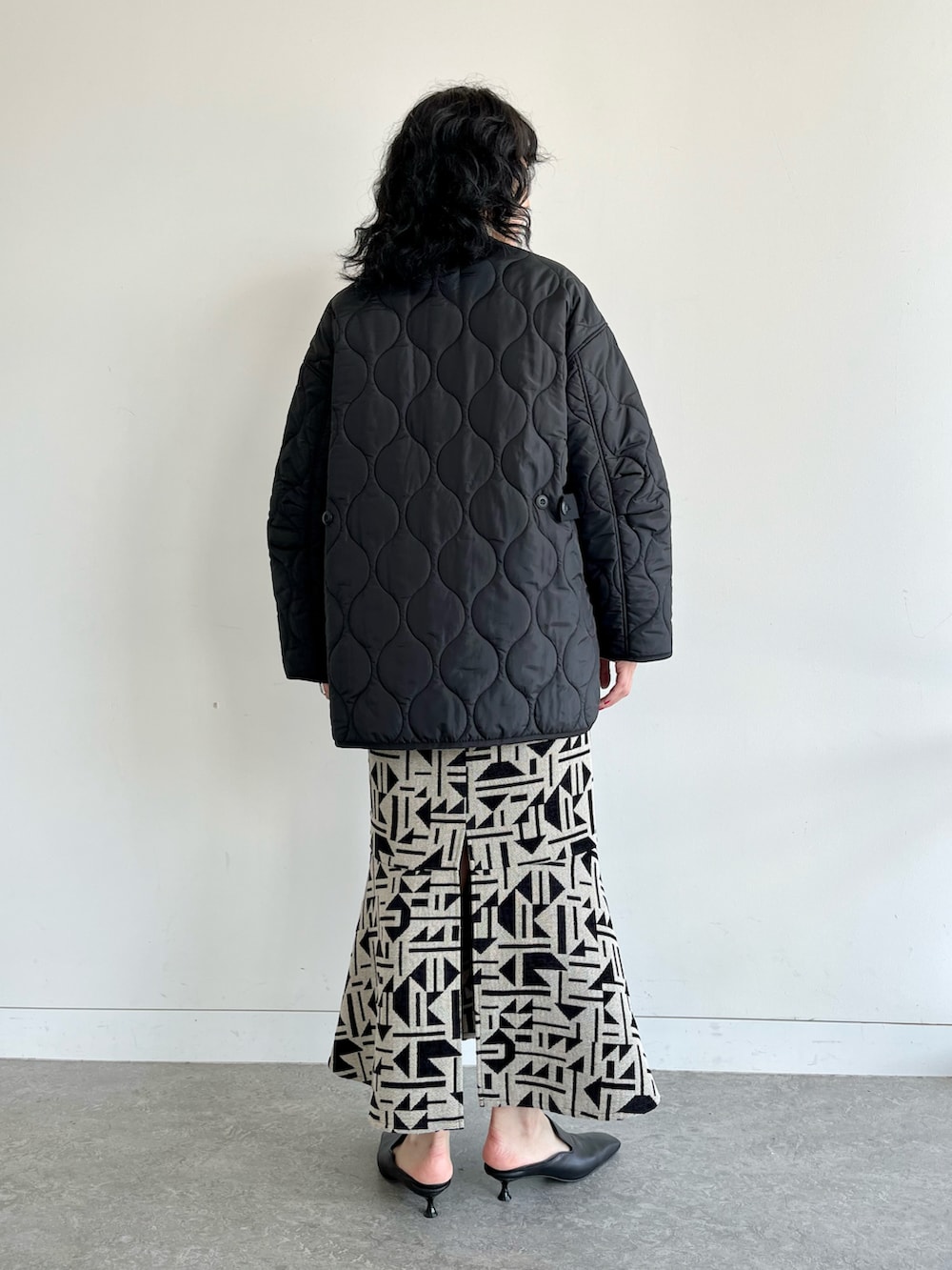 ブラック系のノーカラーコート、ブラック系のスカート、ホワイト系のTシャツ/カットソーを着用したレディースの秋コーディネートの3枚目の写真