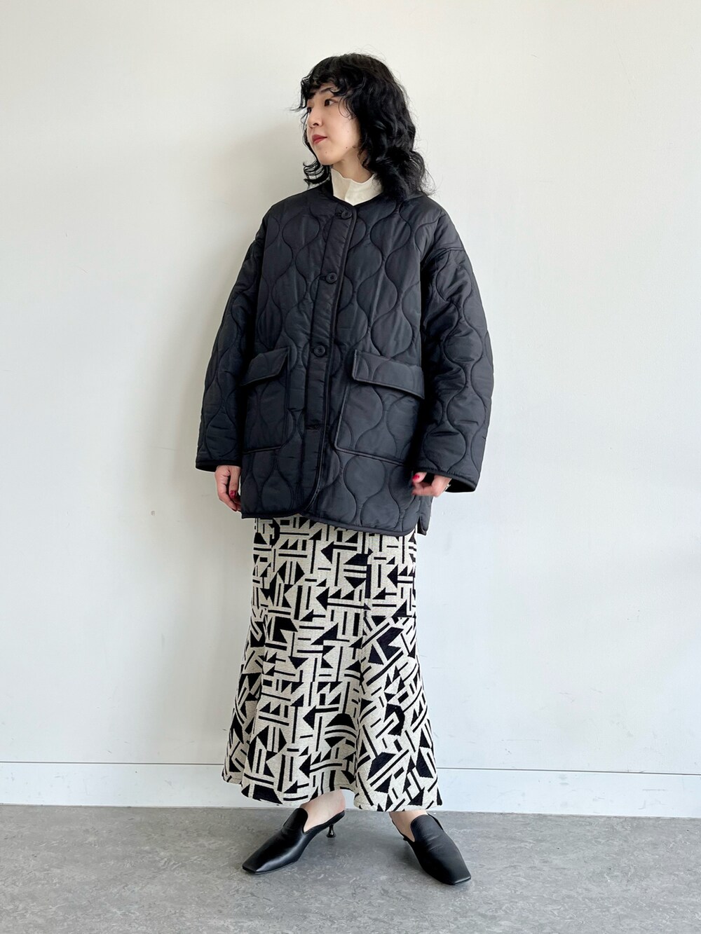 ブラック系のノーカラーコート、ブラック系のスカート、ホワイト系のTシャツ/カットソーを着用したレディースの秋コーディネートの2枚目の写真