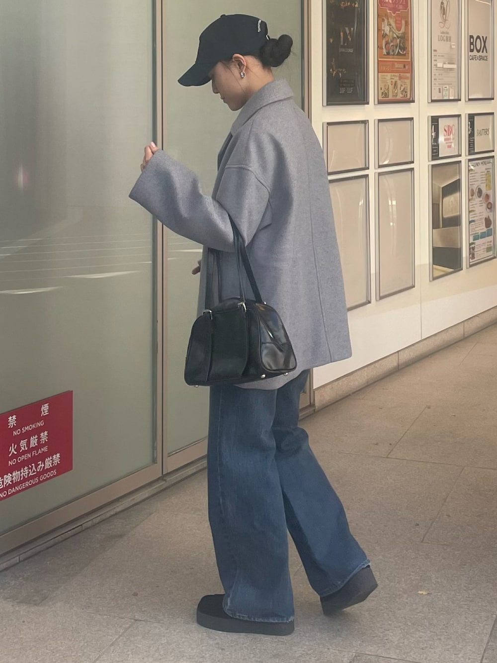 グレー系のピーコート、ブラック系のボストンバッグ、ブルー系のデニムパンツを着用したレディースの秋コーディネートの2枚目の写真