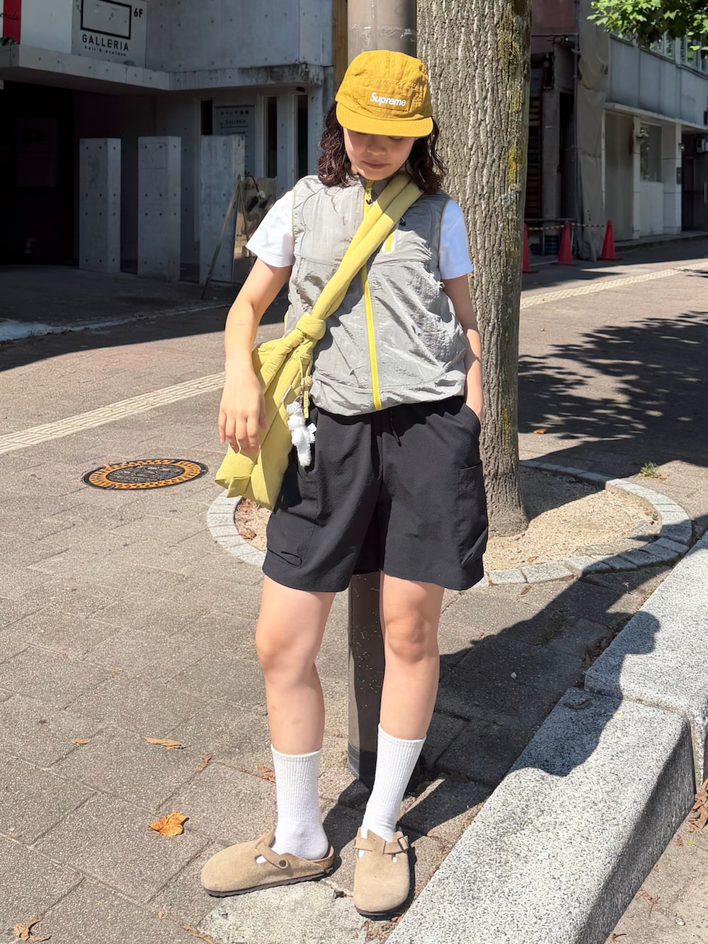 イエロー系のトップス、イエロー系のハンドバッグ、ブラック系のパンツを着用したレディースの夏コーディネートの2枚目の写真