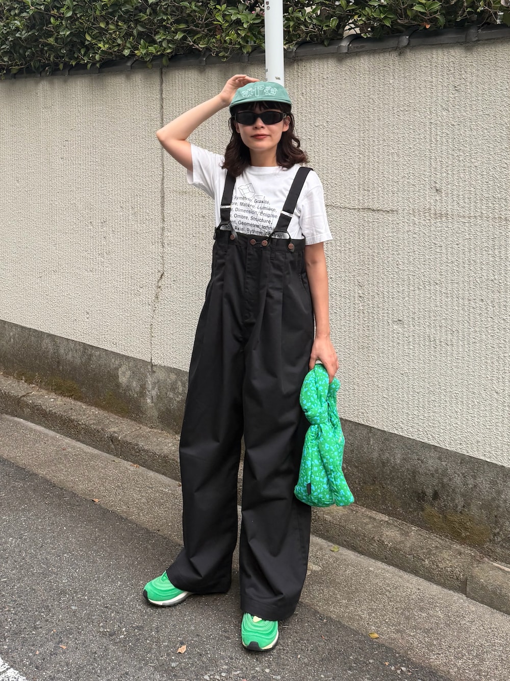 ホワイト系のトップス、ブラック系のチノパンツ、グリーン系のバッグを着用したレディースの夏コーディネートの2枚目の写真