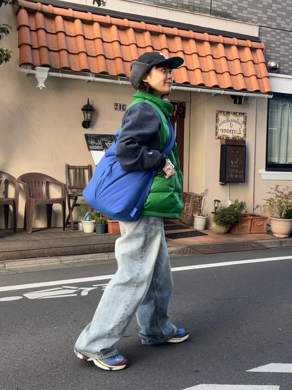 ブルー系のハンドバッグ、グリーン系のダウンベスト、ブルー系のデニムパンツを着用したレディースの秋コーディネートの2枚目の写真