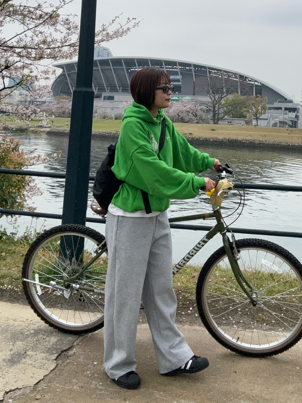 グリーン系のパーカー、グレー系のスウェットパンツ、ブラック系のスニーカーを着用したレディースの春コーディネートの2枚目の写真