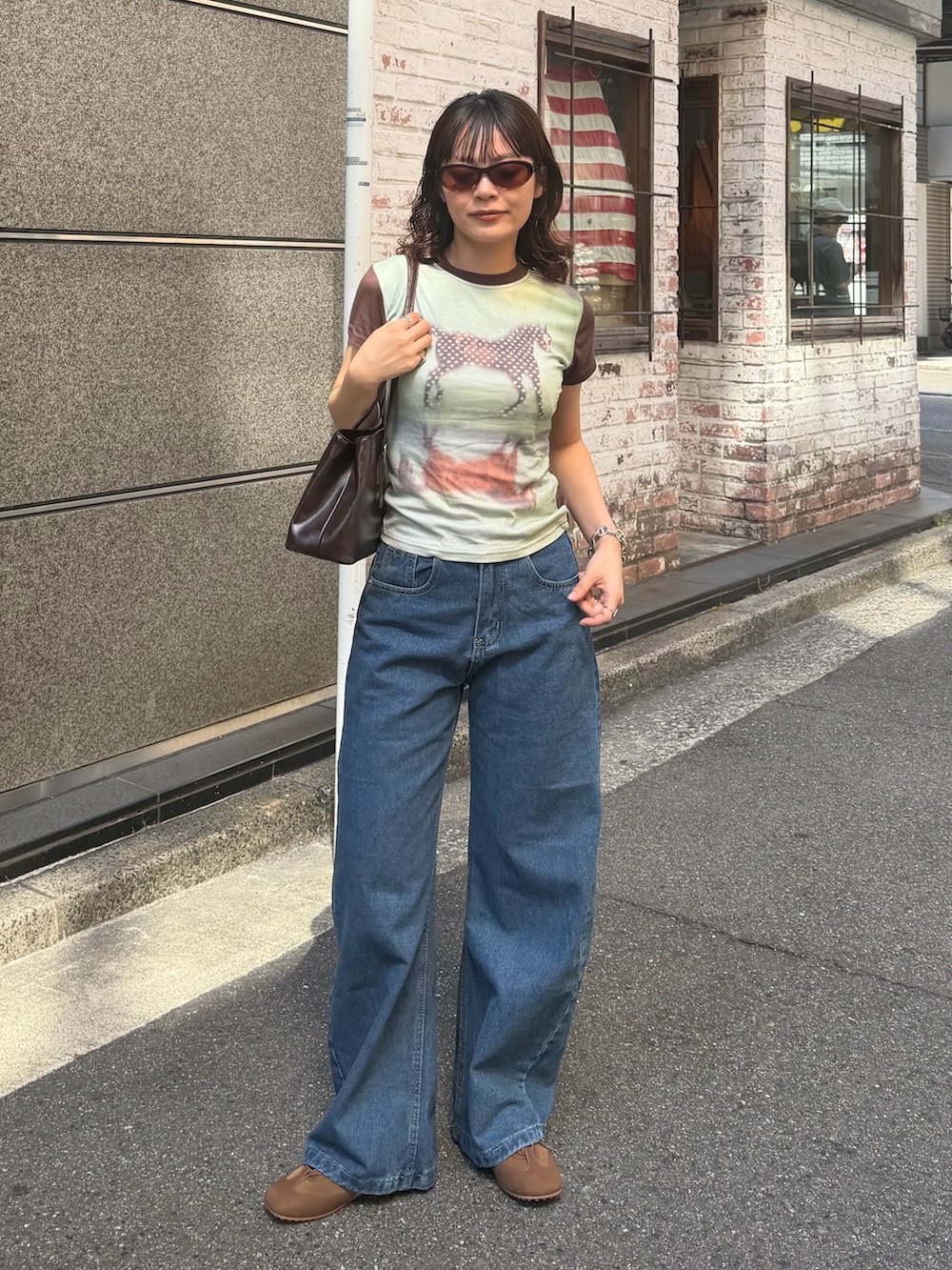 グリーン系のトップス、ブルー系のデニムパンツ、ブラック系のバッグを着用したレディースの夏コーディネートの2枚目の写真