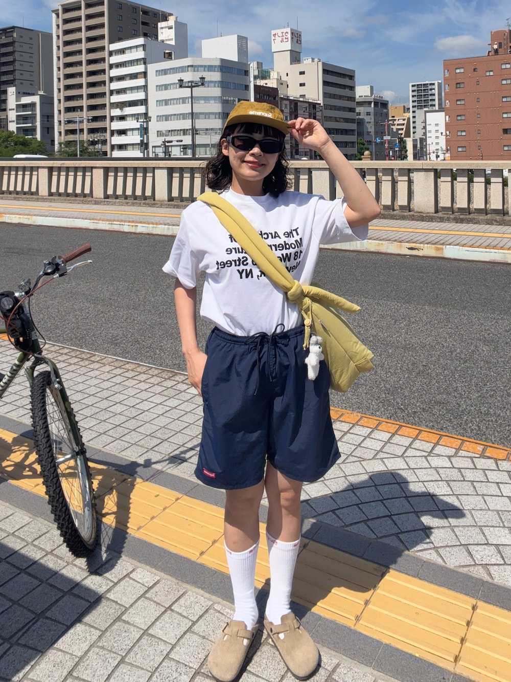 イエロー系のハンドバッグ、ベージュ系のサンダル、ホワイト系のTシャツ/カットソーを着用したレディースの夏コーディネートの2枚目の写真