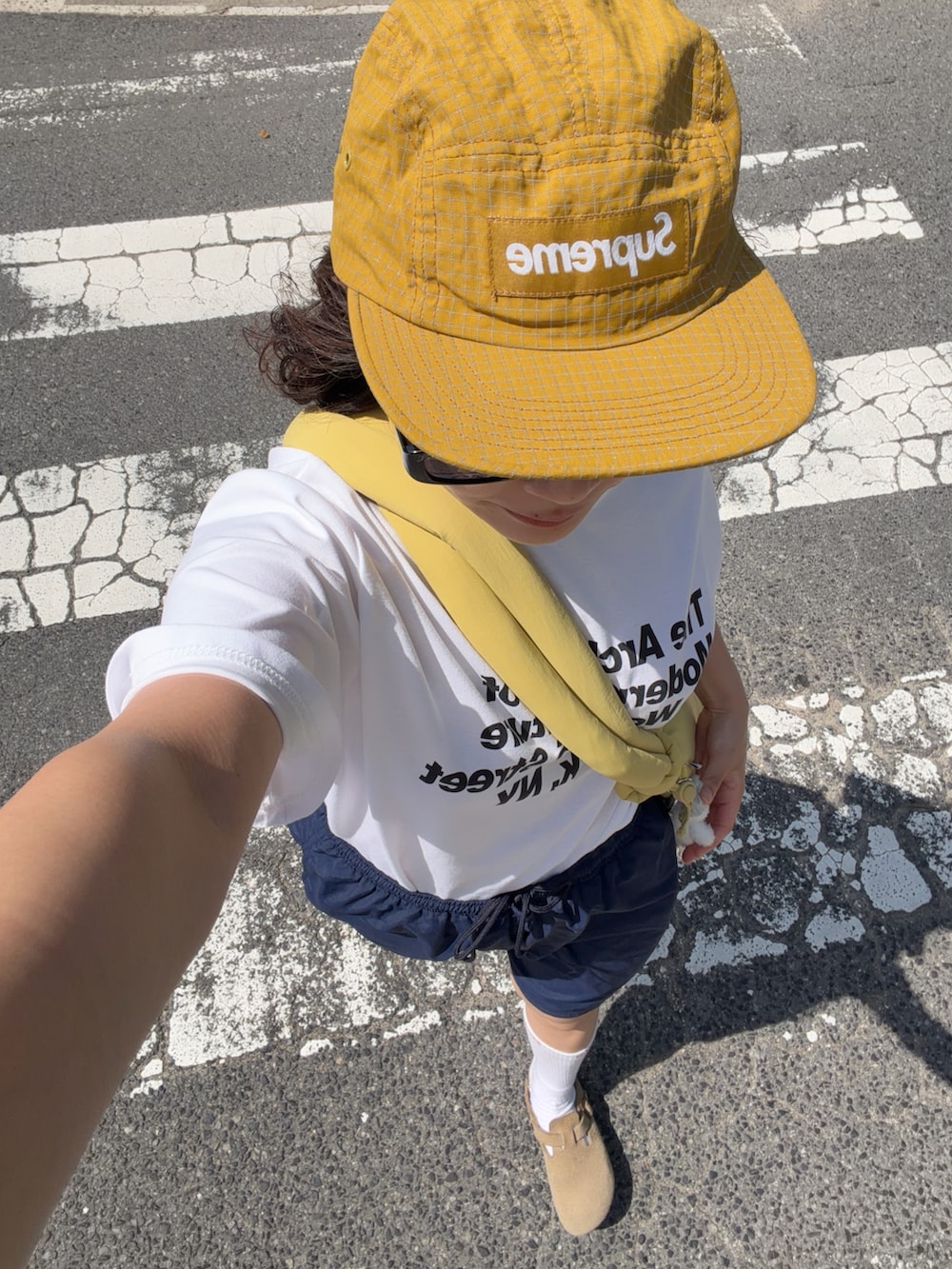 イエロー系のハンドバッグ、ベージュ系のサンダル、ホワイト系のTシャツ/カットソーを着用したレディースの夏コーディネートの3枚目の写真