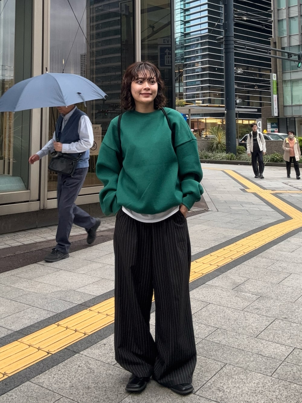 グリーン系のスウェット、ブラック系のバックパック/リュック、ブラック系のスラックスを着用したレディースの春コーディネートの3枚目の写真