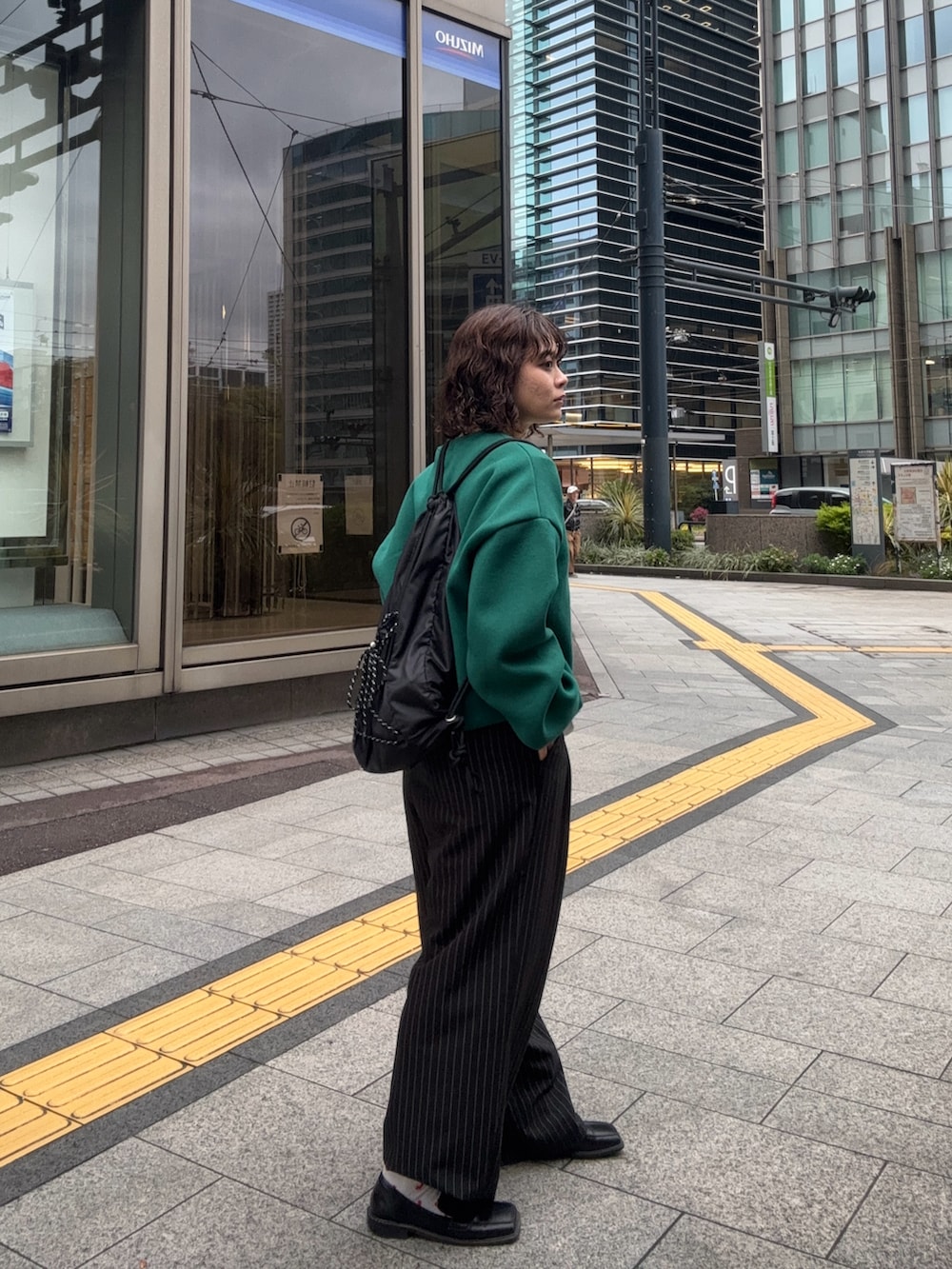 グリーン系のスウェット、ブラック系のバックパック/リュック、ブラック系のスラックスを着用したレディースの春コーディネートの2枚目の写真