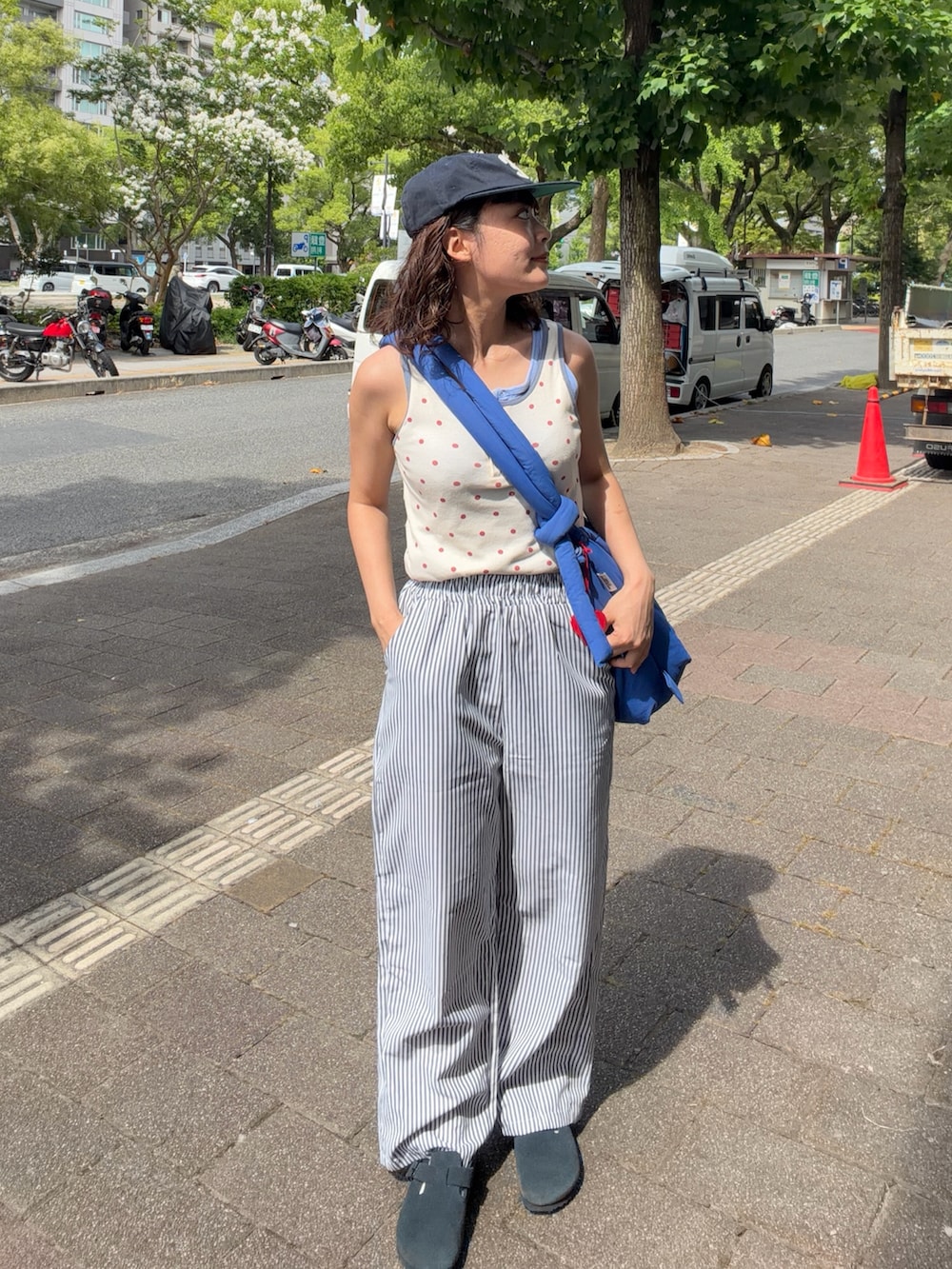 レッド系のタンクトップ、ブルー系のハンドバッグ、ホワイト系のパンツを着用したレディースの夏コーディネートの2枚目の写真