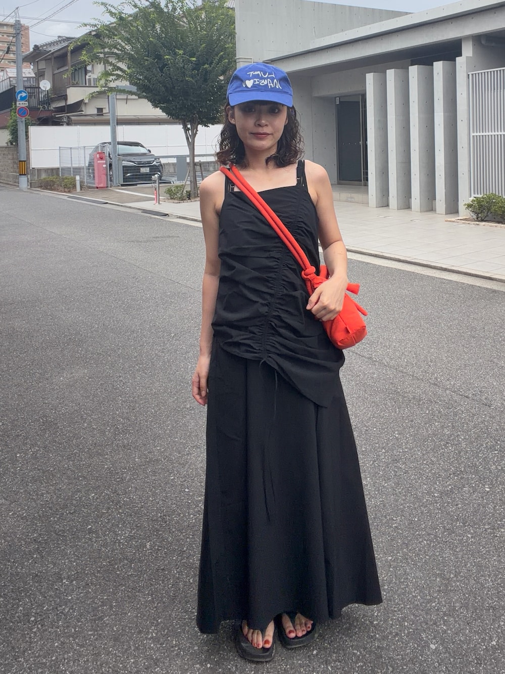 ブラック系のワンピース、オレンジ系のハンドバッグ、ブラック系のサンダルを着用したレディースの夏コーディネートの2枚目の写真