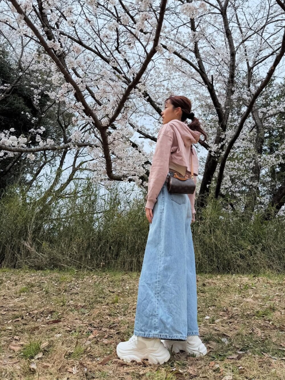 ピンク系のスウェット、ブルー系のデニムパンツ、ホワイト系のスニーカーを着用したレディースの春コーディネートの2枚目の写真