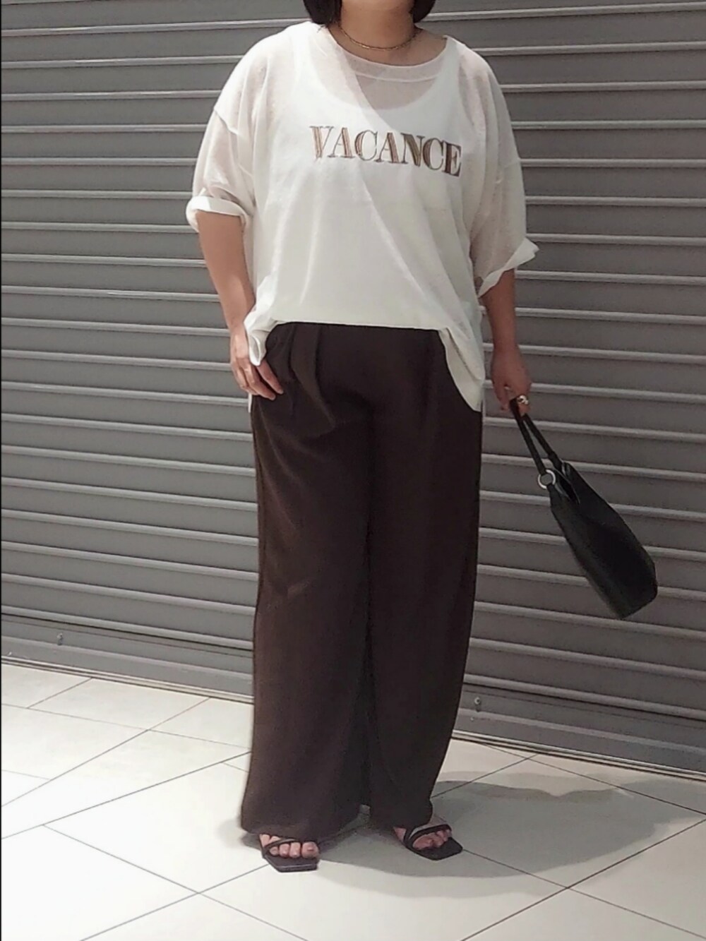 ホワイト系のニット/セーター、ブラウン系のスラックス、ブラック系のハンドバッグを着用したレディースの夏コーディネートの3枚目の写真