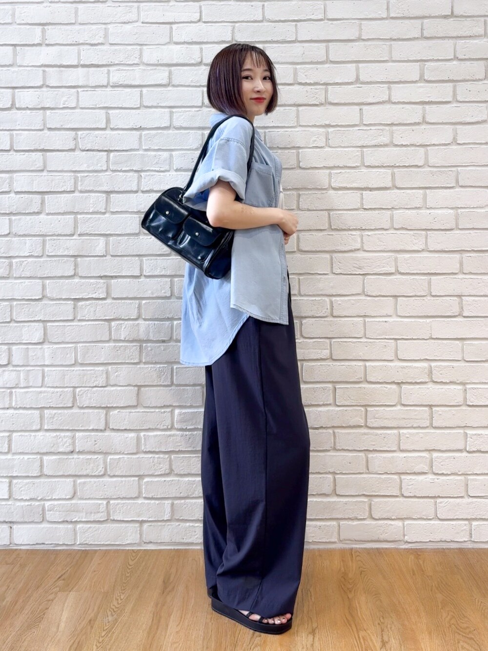 ブルー系のシャツ/ブラウス、ブラック系のサンダル、ブラック系のボストンバッグを着用したレディースの夏コーディネートの2枚目の写真