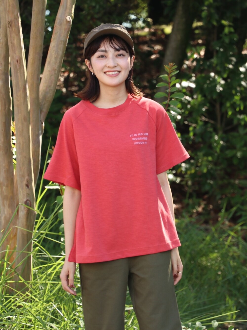 レッド系のTシャツ/カットソー、グリーン系のキャップを着用したレディースの春コーディネートの2枚目の写真