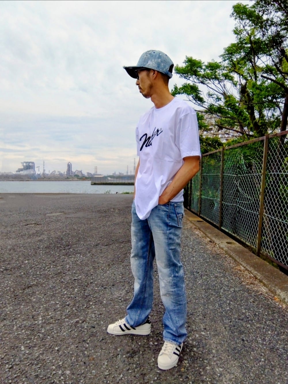 ブルー系のデニムパンツ、ホワイト系のスニーカー、ホワイト系のTシャツ/カットソーを着用したメンズの夏コーディネートの3枚目の写真