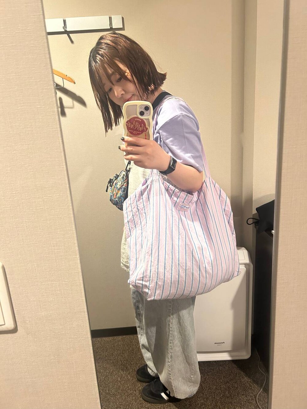 パープル系のトートバッグ、ブラック系のスニーカー、ブルー系のデニムパンツを着用したレディースの夏コーディネートの7枚目の写真
