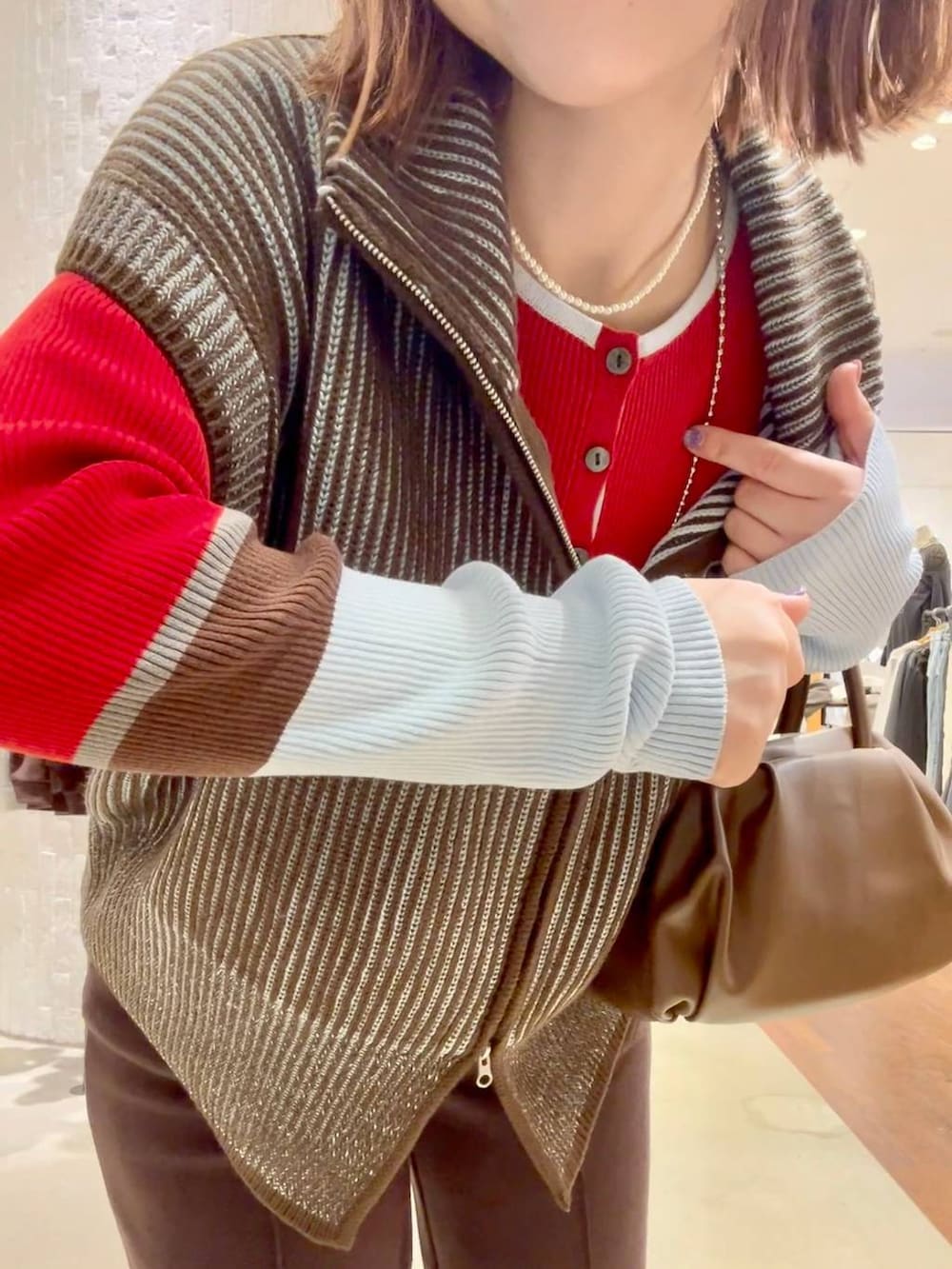 レッド系のニット/セーター、ブラウン系のショルダーバッグ、ブラック系のスニーカーを着用したレディースの秋コーディネートの7枚目の写真