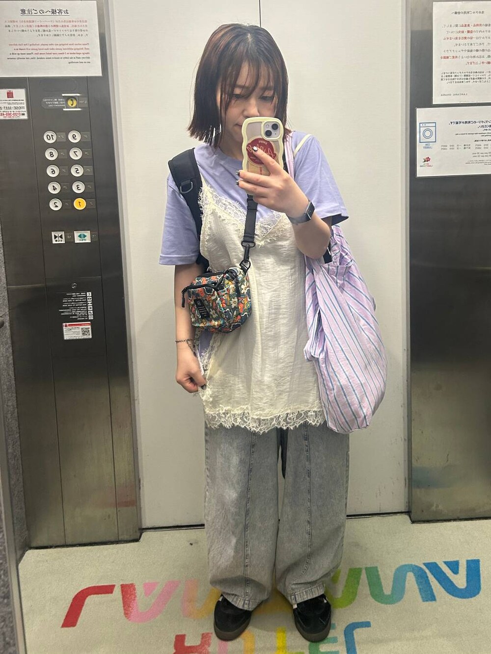 パープル系のトートバッグ、ブラック系のスニーカー、ブルー系のデニムパンツを着用したレディースの夏コーディネートの2枚目の写真